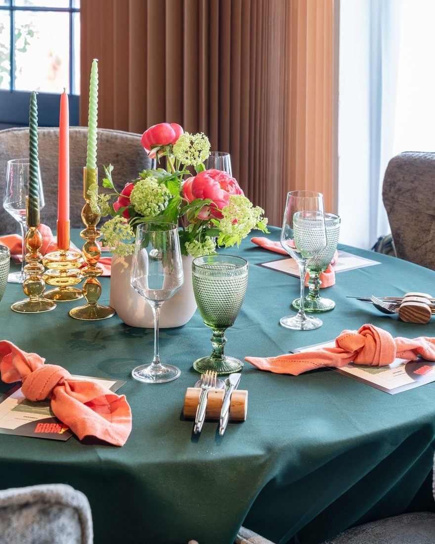 Carbe Diem tablescape with green linens, coral napkins, candles, and fresh florals