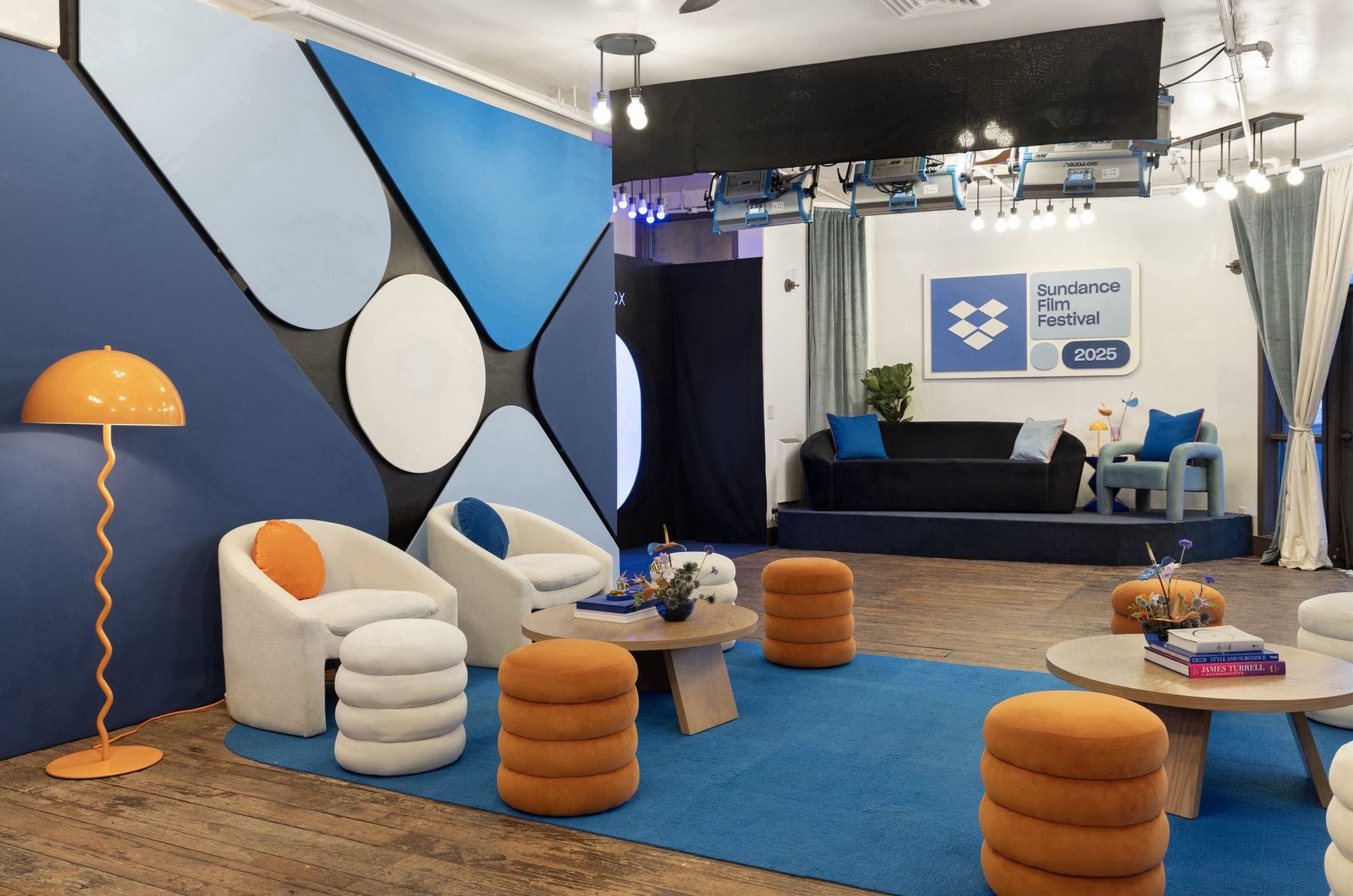 Dropbox x IndieWire lounge at Sundance with a blue rug, orange stools, and an illuminated pegboard wall