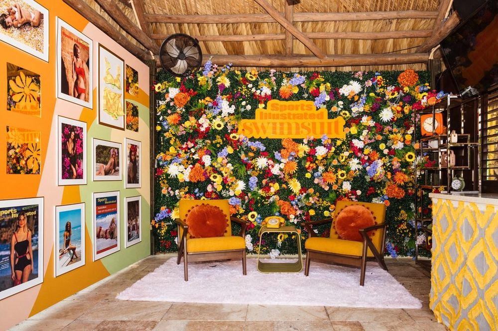 SI Swimsuit cabana with a floral wall, orange chairs, and framed magazine covers